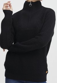 Schwarzer gestrickter Pullover mit hohem Kragen und Reißverschluss, ausgestattet mit gerippten Bündchen und einem strukturierten Muster. Mit einem Logo-Tag akzentuiert.
