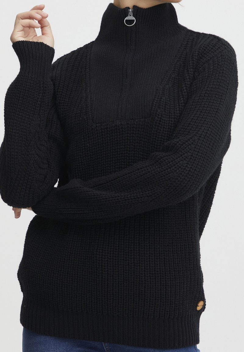 Schwarzer gestrickter Pullover mit hohem Kragen und Reißverschluss, ausgestattet mit gerippten Bündchen und einem strukturierten Muster. Mit einem Logo-Tag akzentuiert.