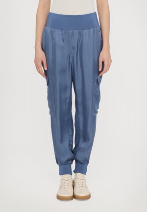 Blå satinjoggingbyxor med en bred elastisk midja, sidofickor och elastiska muddar. Matchas med ljusa sneakers.