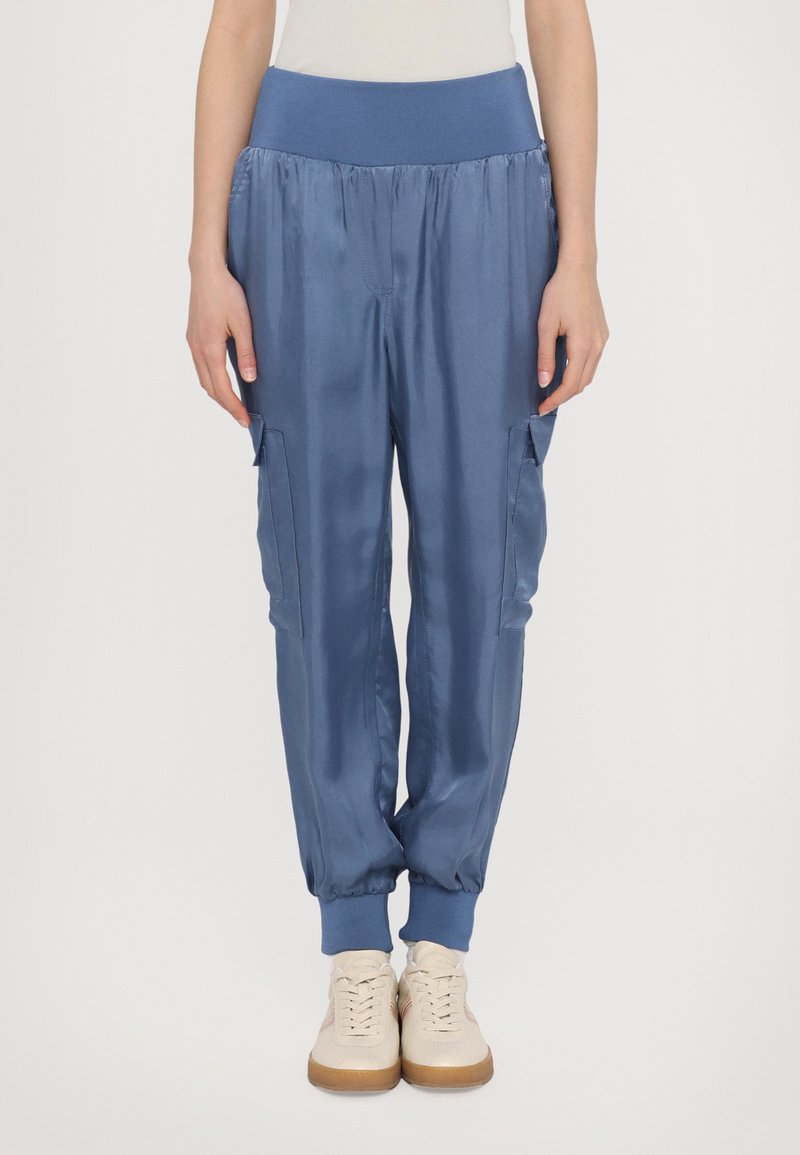 Blauwe satijnen joggingsbroeken met een brede elastische tailleband, zijzakken en elastische manchetten. In combinatie met lichtgekleurde sneakers.
