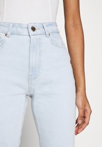 Jeans de tiro alto en azul claro confeccionados en denim. Presenta un cierre de botón, bolsillos frontales y una textura suave con detalles de costura sutiles.