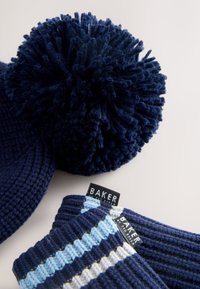 Tengerészkék kötött sapka nagy bojttal és hozzá illő ujjatlan kesztyűk váltakozó kék csíkkal és fekete "BAKER" feliratú címkékkel.