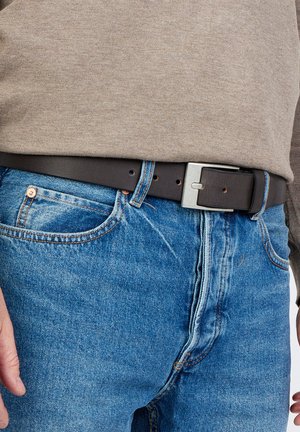 Bruine leren riem met een rechthoekige metalen gesp, gedragen over blauwe denim jeans en een beige langemouwenhemd. Eenvoudige textuur en minimalistisch ontwerp.