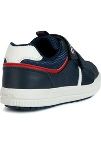 Basket bleue marine avec un dessus en cuir et en maille, accents blancs, bande rouge et sangle Velcro. Dispose d'une surface texturée et d'une semelle en caoutchouc.