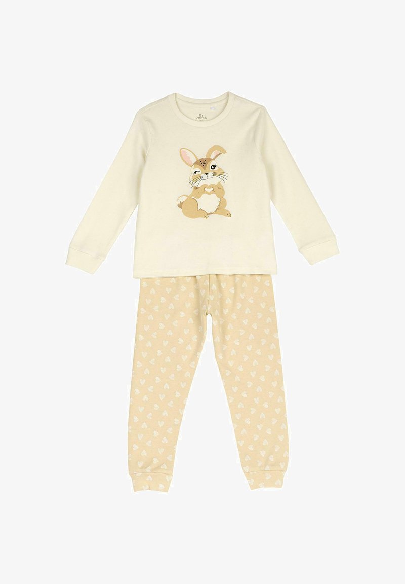 Haut crème à manches longues avec un lapin de dessin animé faisant un clin d'œil en formant un cœur, associé à un pantalon beige couvert de petits cœurs blancs.