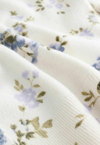 Tissu doux avec une base blanche, présentant de petits motifs floraux bleus et verts, et une surface à nervures texturées.
