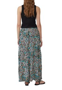 Schwarzes ärmelloses Top kombiniert mit einem langen, gemusterten Rock, der geometrische Designs in Türkis, Braun und Schwarz aufweist und aus fließendem Material besteht.