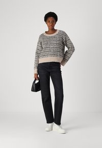 Sweater court à motifs gris avec des accents beiges, associé à un jean droit sombre et des baskets blanches. Tenant un petit sac à main noir.