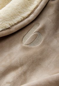Coperta in pile beige con una texture morbida e pelosa. Caratterizzata da un logo ricamato in rilievo e da un bordo in shearling a contrasto.