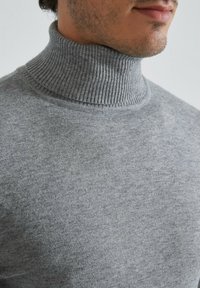 Pull en maille côtelée gris en tissu doux et texturé, doté d'un col en côtes et d'une silhouette ajustée.