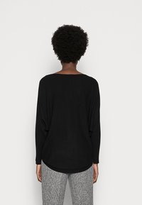 Suéter negro de punto con un escote amplio, hombros caídos y un dobladillo redondeado, combinado con pantalones grises texturizados. Tejido suave, ajuste holgado.