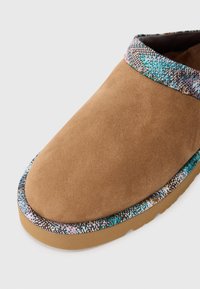 Chaussure en suede marron à enfiler avec une bordure texturée multicolore et une semelle en caoutchouc beige. Surface lisse avec un design de bout arrondi.