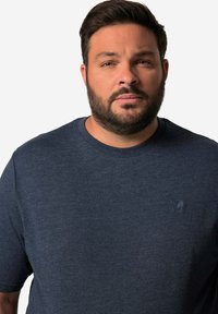 Granatowy T-shirt z okrągłym dekoltem wykonany z miękkiej bawełny, z małym wytłoczonym logo na piersi i krótkimi rękawami. Gładka tekstura.