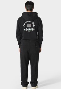 Černá mikina s kapucí se zadním grafickým designem znázorňujícím závodní auto a text. Spárováno s odpovídajícími černými kalhotami. Měkká tkanina, volný střih.