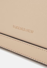 Beżowy materiał syntetyczny z wytłoczonym logo "FOREVER NEW", czarnymi przeszyciami i gładką, matową teksturą. Kompaktowy design.