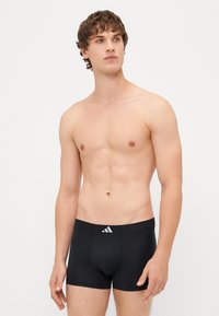 Boxers pretos ajustados, feitos de um material suave, com um logótipo branco da Adidas na cintura. Comprimento de perna curto.