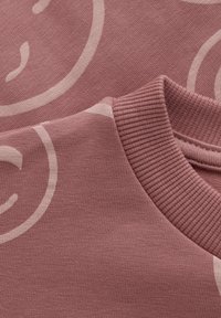 Roze sweatshirt met een geribbelde ronde hals, zachte textuur en een groot lichtroze smiley-gezicht patroon over de stof.