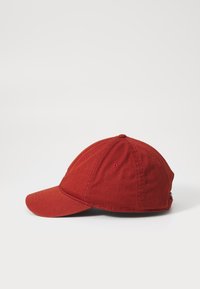 Piros baseball sapka ívelt karimával. Texturált szövetből készült, szellőzőnyílásokkal és hátul állítható pánttal van ellátva.