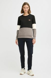 Felpa color block in nero, grigio e crema con collo rotondo; misto cotone, texture morbida; abbinata a pantaloni cargo blu e sneakers.