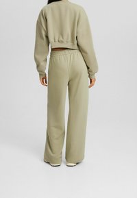 Olivgrön kort sweatshirt med sänkta axlar, kombinerad med lösa, högmidjade byxor i samma material och färg. Slät textur.