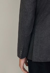 Blazer grigio in lana con colletto a scollo a V, forma strutturata e quattro bottoni decorativi sui polsini. Tessuto morbido con vestibilità su misura.