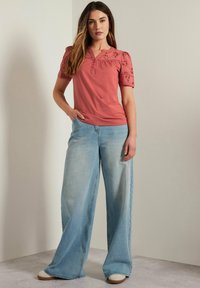Blusa di cotone rosa antico con maniche corte a palloncino ricamate, abbinata a jeans in denim blu chiaro a gamba larga e scarpe beige con zeppa.