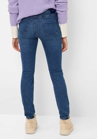 Smal blå jeans lavet af denim, med baglommer og en mid-rise talje. Båret med en lavendelstriktrøje og beige ankelstøvler.
