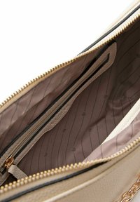 Interno di una borsa in pelle beige con una cerniera dorata, dotato di una tasca foderata e un tessuto liscio con motivo. Accenti in metallo dorato visibili.