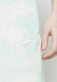 Bavlněné tričko v světle mátové barvě s tie-dye vzorem. Obsahuje malé bílé vyšívané logo Nike na levé straně.