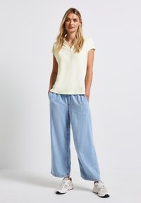 Maglietta polo corta di colore giallo chiaro abbinata a pantaloni in denim azzurro chiaro larghi e sneaker bianche. Tessuto morbido e vestibilità rilassata.