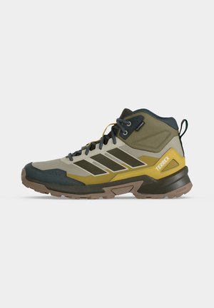 Buty trekkingowe o średniej wysokości w zielonym, żółtym i brązowym kolorze z czarnymi sznurówkami, wytrzymałą podeszwą i logo "Terrex" z boku.