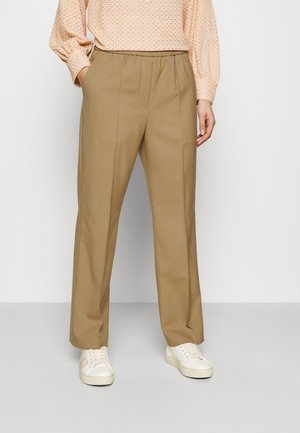 Pantalons larges beiges avec une taille élastique, design ajusté, texture lisse, associés à des baskets blanches.