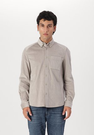 Light brown button-up shirt with vertical stripes, a chest pocket, and a structured collar, made from a textured fabric. Worn with dark jeans.