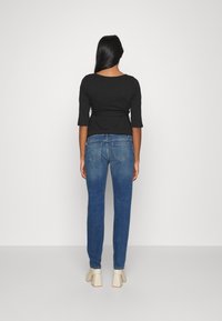 Svart topp med trekvartsärmar, blå jeans med bakfickor, något avsmalnande passform, i kombination med beige klackskor med blockklack.