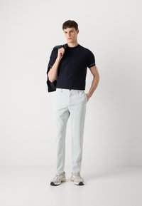Tricou navy cu mânecă scurtă și accente albe, pantaloni light blue și pantofi sport bej. Modelul poartă o jachetă navy pe umăr.