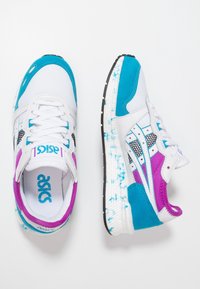 White athletic shoes featuring blue, purple, and black accents. Includes mesh and suede materials with a patterned sole and logo detailing.