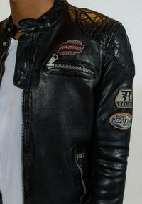 Veste de moto en cuir noir avec des accents matelassés aux épaules, quincaillerie en argent, poches zippées et écussons de course brodés.