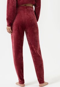 Scharlaken fluwelen joggerbroek met een aansluitende tailleband en taps toelopende broekspijpen. Zachte textuur met minimale naden, ontworpen voor comfort en casual gebruik.