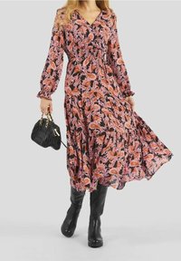Vestido de manga larga con estampado floral en negro, rosa y naranja, con cintura ajustada. Combinado con botas altas negras hasta la rodilla y un bolso negro pequeño.