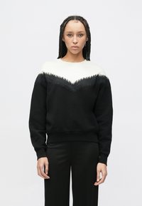 Czarna bluza z białym dekoltem w kształcie litery V z frędzlami. Ściągacze na mankietach i dole, luźny krój, fason zakładany przez głowę.