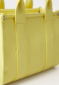 Geltona odinė rankinė su iškilniu "VALENTINO" logotipu, struktūrizuota forma ir dviem rankenomis. Tekstūruotas paviršius su matomomis siūlėmis.