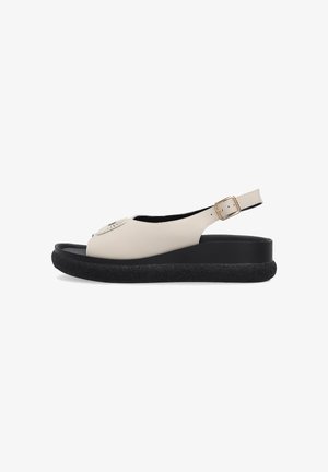 Beige sandal med åben tå, sort tekstureret plateau-sål og justerbar bagrem med guldfarvet spænde, set fra siden på hvid baggrund.