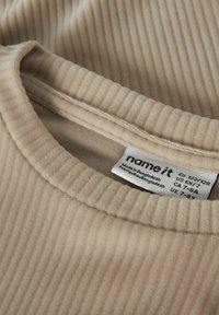 Beige geribd shirt met lange mouwen, een ronde halslijn en een label met maatinformatie dat in de kraag is genaaid.