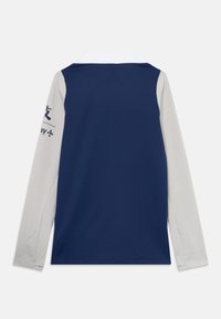 Långärmad polo skjorta med marinblå baksida, ljusgrå ärmar som har mörkblå text på en ärm, och en vit krage.