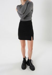 Grijze geribbelde lange mouwen trui, zwarte mini rok met een zijsplit en zwarte veterboots met een grof profiel. Glad textuur, aansluitend ontwerp.