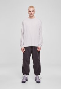 Svetlosivý top s dlhým rukávom, čierne voľné nohavice a sivé tenisky s textúrovanými detailmi. Zobrazené na neutrálnom pozadí.