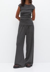 Top grigio a coste con maniche corte abbinato a pantaloni grigi a gamba larga, entrambi caratterizzati da una texture morbida e un design casual. Scarpe marroni completano il look.