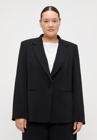 Črni tailorski blazer iz gladkega blaga, ki ima urezan ovratnik, zapiranje z enim gumbom in dva sprednja žepa z diskretnimi pipi.