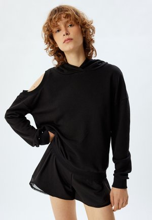 Zwarte oversized sweatshirt met open schouderontwerp, capuchon en lange mouwen. Gemaakt van zachte stof, gecombineerd met bijpassende zwarte shorts.