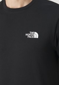 Czarny bawełniany t-shirt z okrągłym dekoltem, z małym białym logo "THE NORTH FACE" po lewej górnej stronie.
